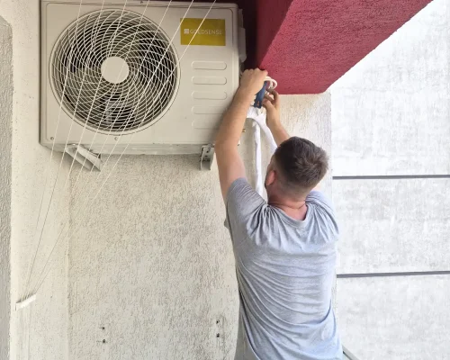Tehnician montând unitatea externă a unui aparat de aer condiționat marca Goldsense pe peretele unui balcon, conectând traseul frigorific izolat.